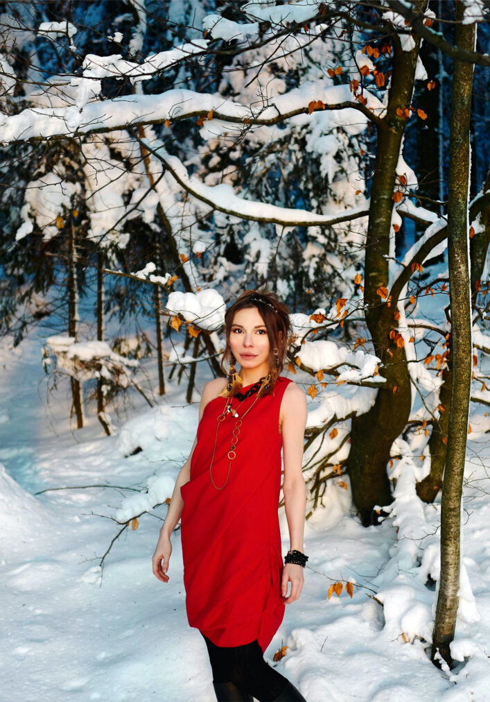 martha may standing in a red cocktail dress in a winter forest